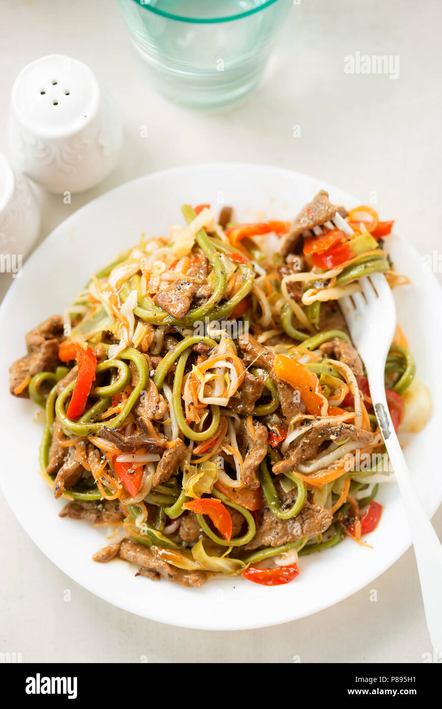 Peperoncino tagliatelle di manzo. Wok fritto in carni bovine il tamarindo e la salsa di soia con tagliatelle verdi, i germogli di soia, carote e peperoni rossi Foto Stock