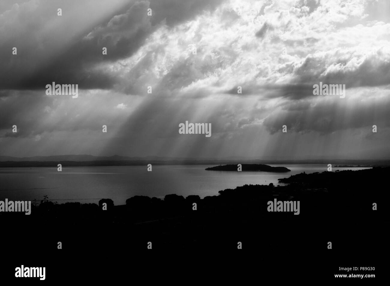 Raggi di sole che fuoriesce attraverso le nuvole sopra un isola in un lago Foto Stock