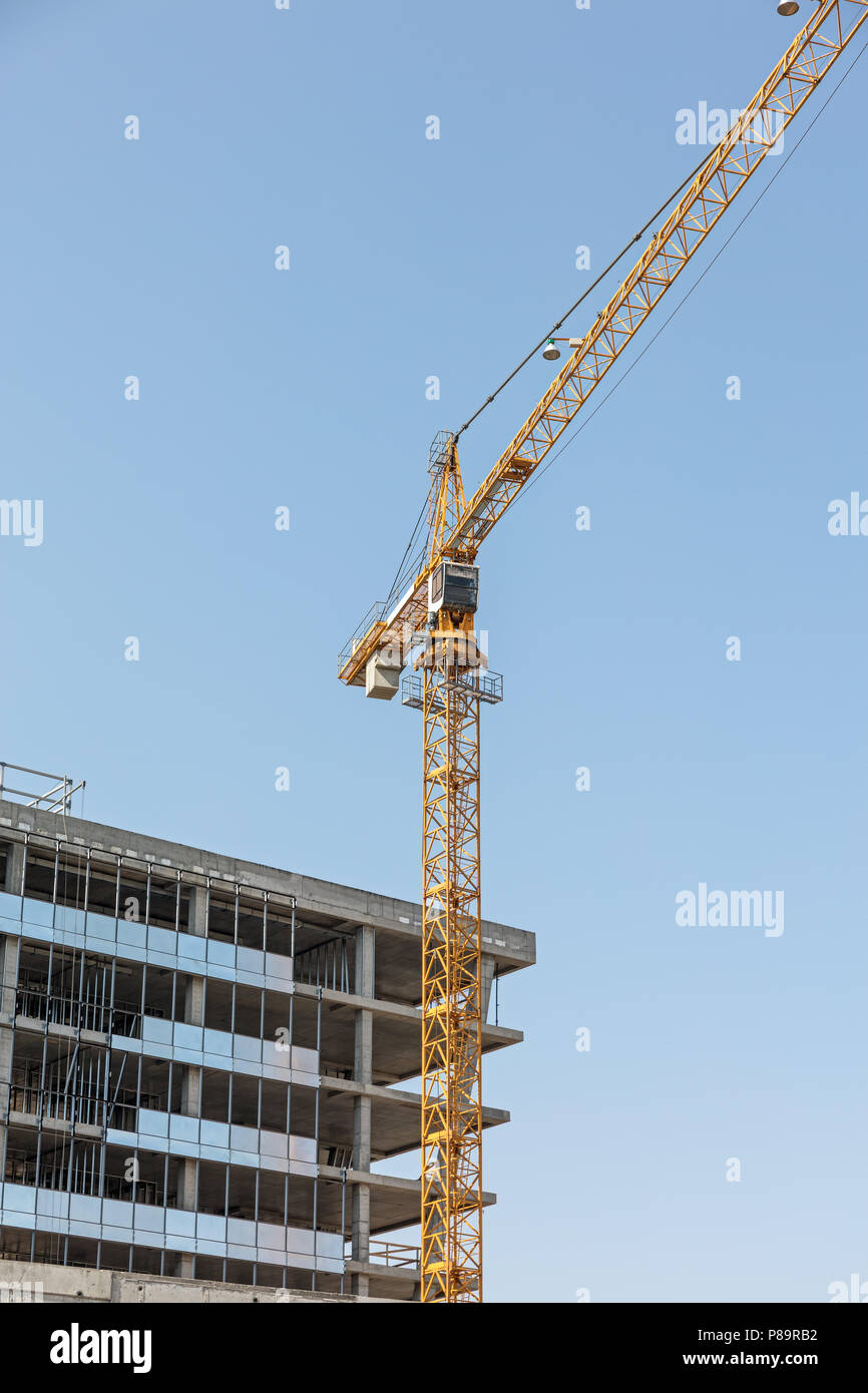 Un edificio in calcestruzzo di colore giallo e di gru a torre contro il cielo blu sullo sfondo Foto Stock