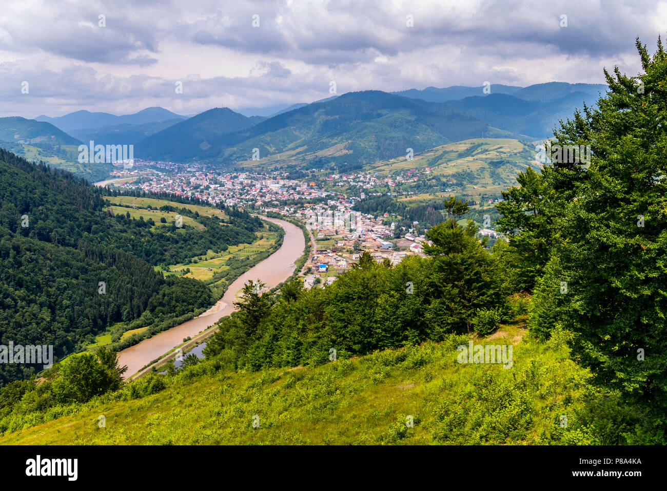 Una vista pittoresca di un villaggio rurale e un fiume veloce contro lo sfondo di alte montagne verdi . Per il vostro design Foto Stock