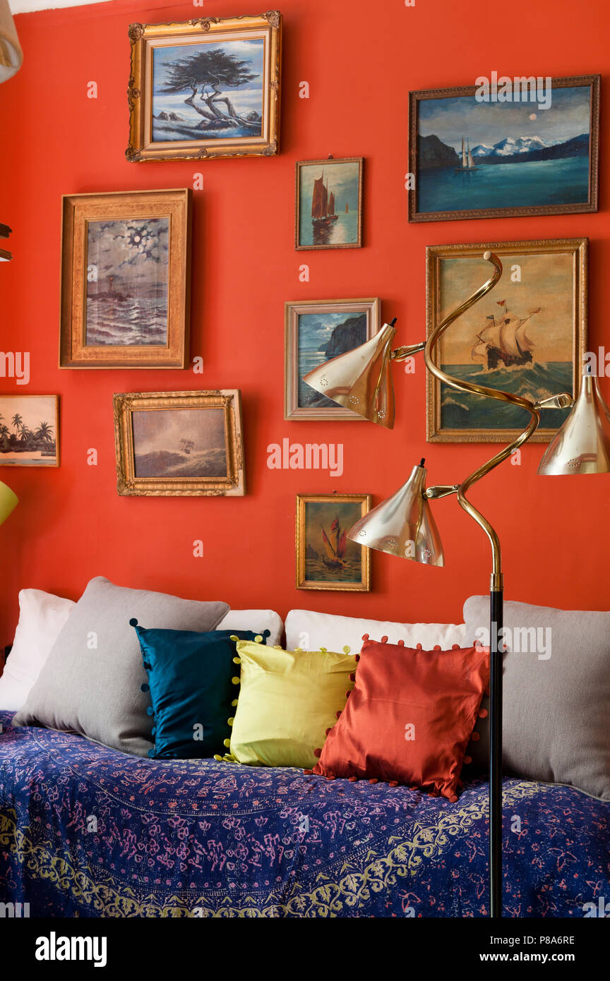 Una collezione di dipinti paesaggi marini sulla parete rossa sopra letto da giorno. La lampada da terra è 1940s Foto Stock
