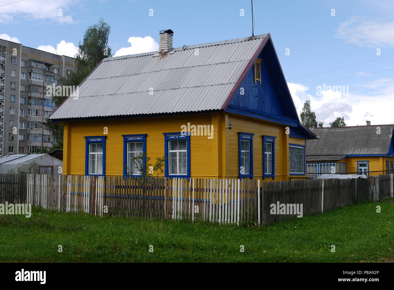 Bel colore giallo casa rurale con un recinto su uno sfondo urbano di edifici ad alta e cielo blu. . Per il vostro design Foto Stock