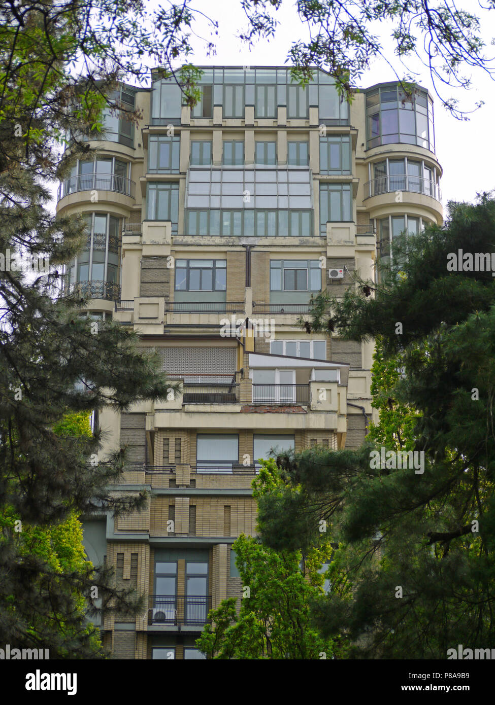 Edificio futuristico nascose dietro i rami degli alberi ad alta densità. Il colore marrone del rivestimento e lo scintillio delle finestre sono disposti splendidamente aga Foto Stock