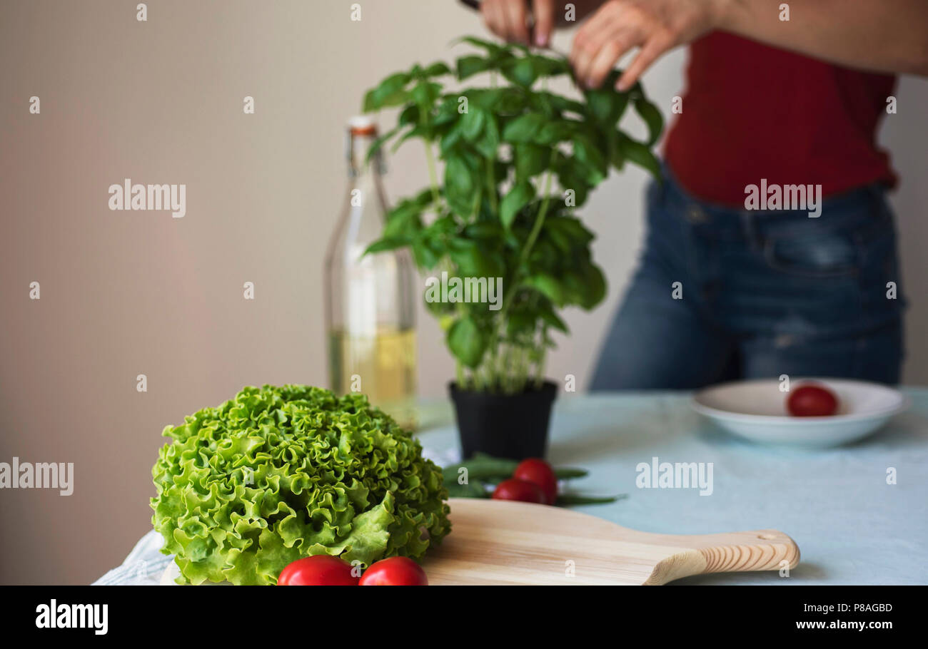 Giovane donna che indossa jeans cucina vegetariana sana detox cibo. Ingredienti e preparazione per una sana cucina italiana Foto Stock