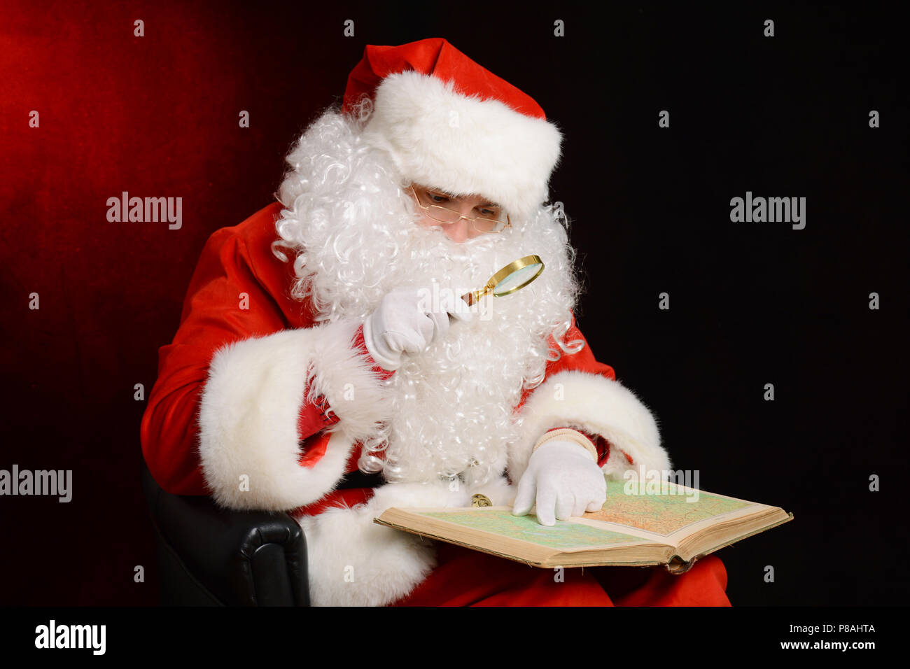 Santa Claus tenendo la lente di ingrandimento e guardando la mappa. Santa azienda mappa sul suo giro Foto Stock