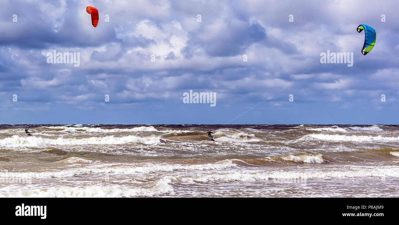 Due kitesurfisti stanno cavalcando le onde del Mar Baltico nei pressi di Venspils spiaggia sotto il cielo nuvoloso. Divertimento in mare. Sport estremo kitesurf. Foto Stock