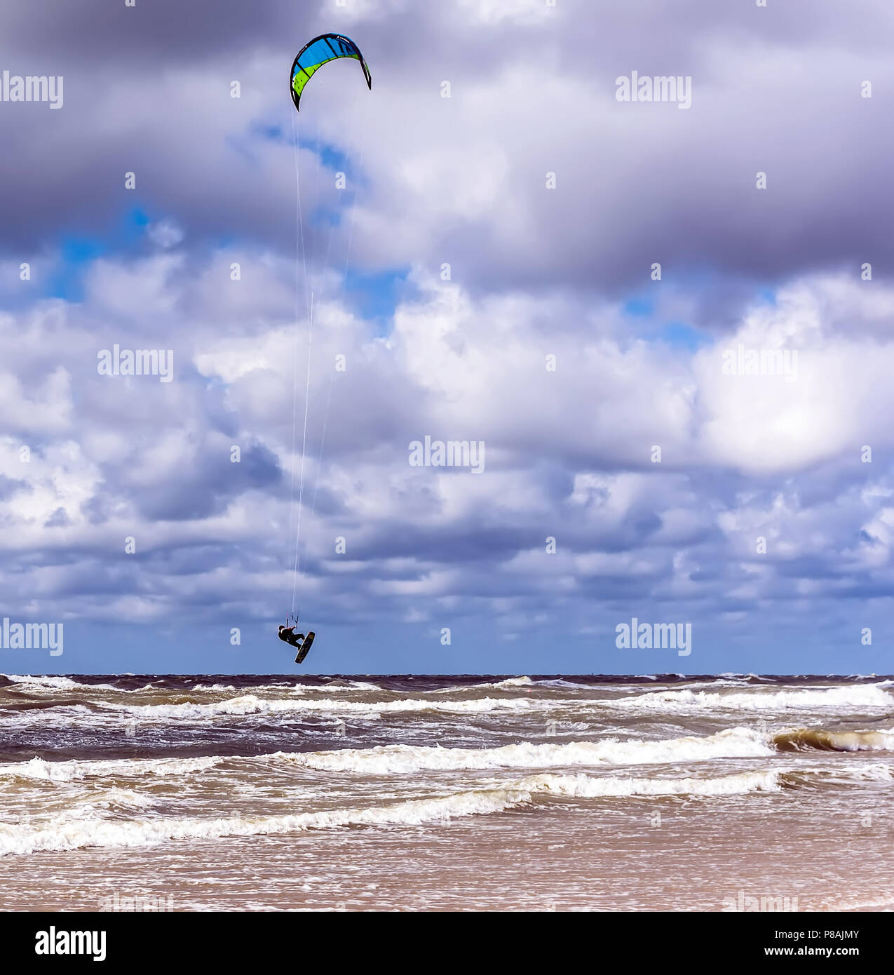 Kitesurfer saltare in aria in alto al di sopra delle onde del Mar Baltico nei pressi di Venspils spiaggia sotto il cielo nuvoloso. Divertimento in mare. Sport estremo kitesurf. Foto Stock