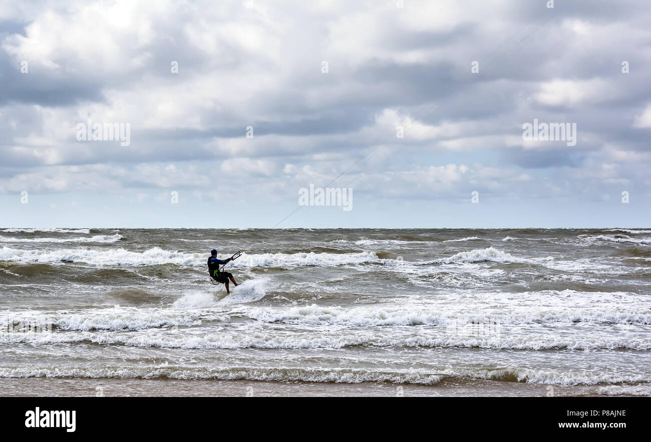 Kitesurfer è cavalcare le onde del mare Baltico nei pressi di Venspils spiaggia sotto il cielo nuvoloso. Divertimento in mare. Sport estremo kitesurf. Foto Stock
