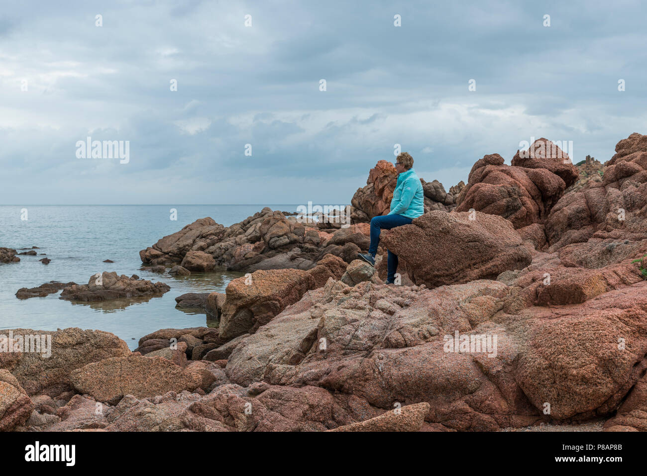 Adulto donna seduta sulle rocce di isola rossa la costa di lettura dell'isola Sardegna appartiene a Italia Foto Stock