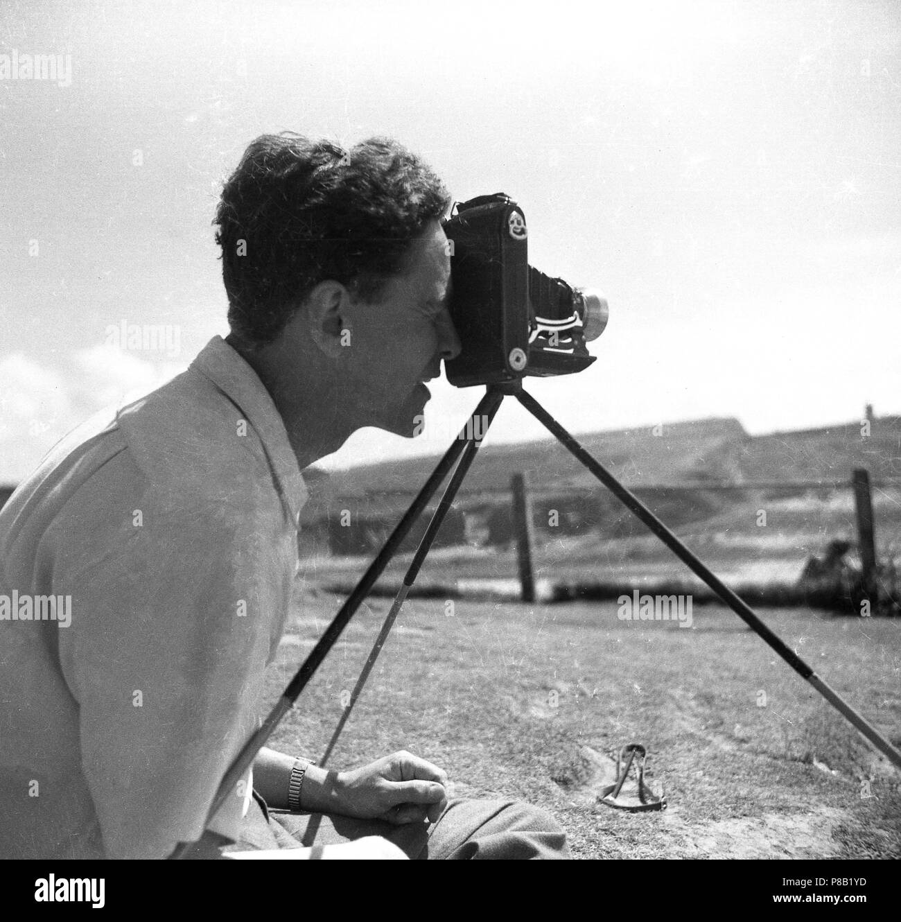 Degli anni Cinquanta, storico, uomo scattare una fotografia al di fuori con un film di piegatura fisso della telecamera su un treppiede, Inghilterra, Regno Unito. La figura mostra la telecamera nella posizione dispiegata. Tali telecamere sono stati popolari con appassionati come essi erano portatili rispetto ai più grandi, le fotocamere più pesante ma ancora usato un medio formato pellicola, un film di grandi dimensioni, (6 x9) quindi di ottenere una migliore qualità di foto. Foto Stock