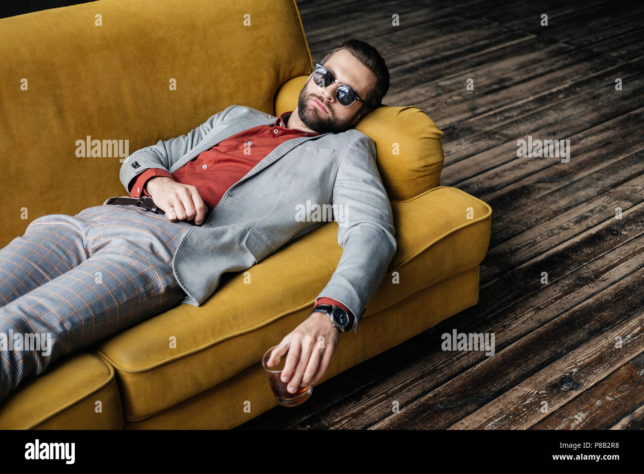 Elegante uomo ubriaco in occhiali da sole tenendo un bicchiere di whiskey e  sdraiato sul divano giallo Foto stock - Alamy