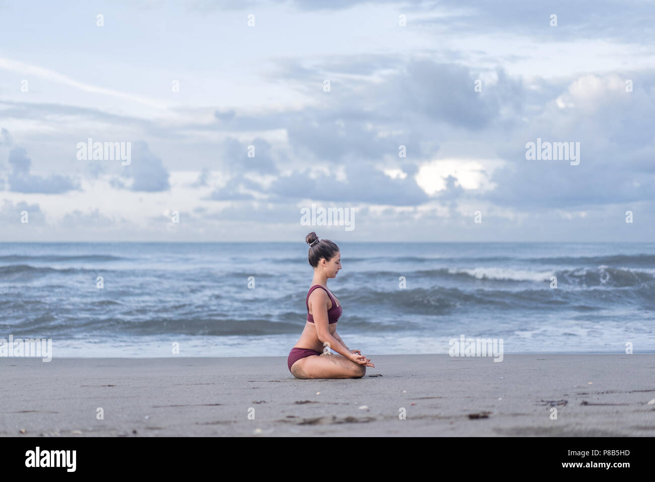 Vista laterale di montare la giovane donna meditando in lotus pongono (padmasana) con gyan mudra sulla riva del mare Foto Stock