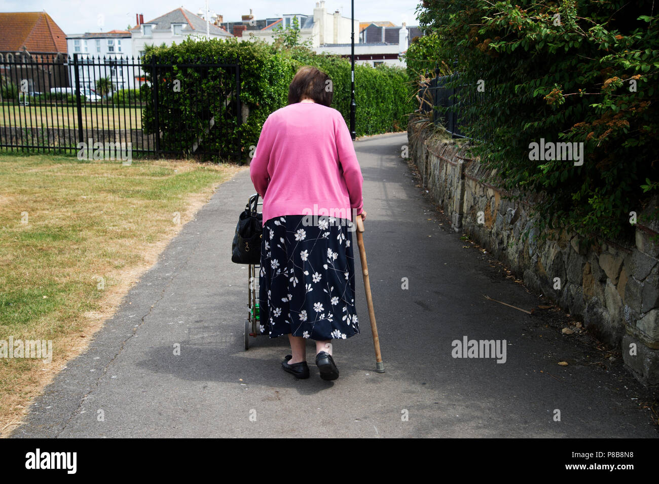 Bognor Regis, Sussex. Una donna anziana che cammina con un bastone e spinge il suo acquirente. Foto Stock