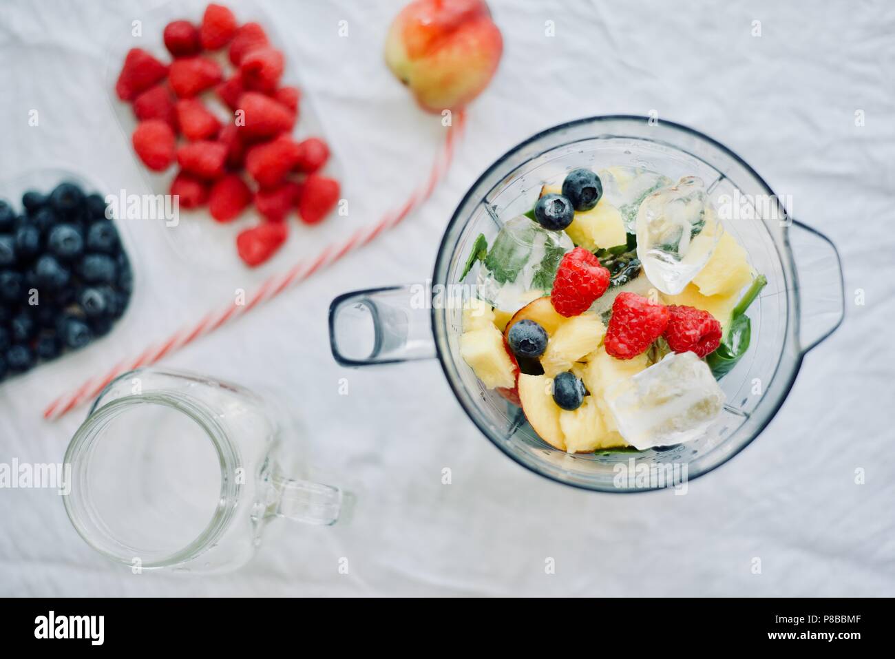 Flat-lay di un frullatore e cibi freschi stagionali di bacche e frutti su sfondo bianco, cottura preparare frullati, detox, sano mangiar pulito Foto Stock