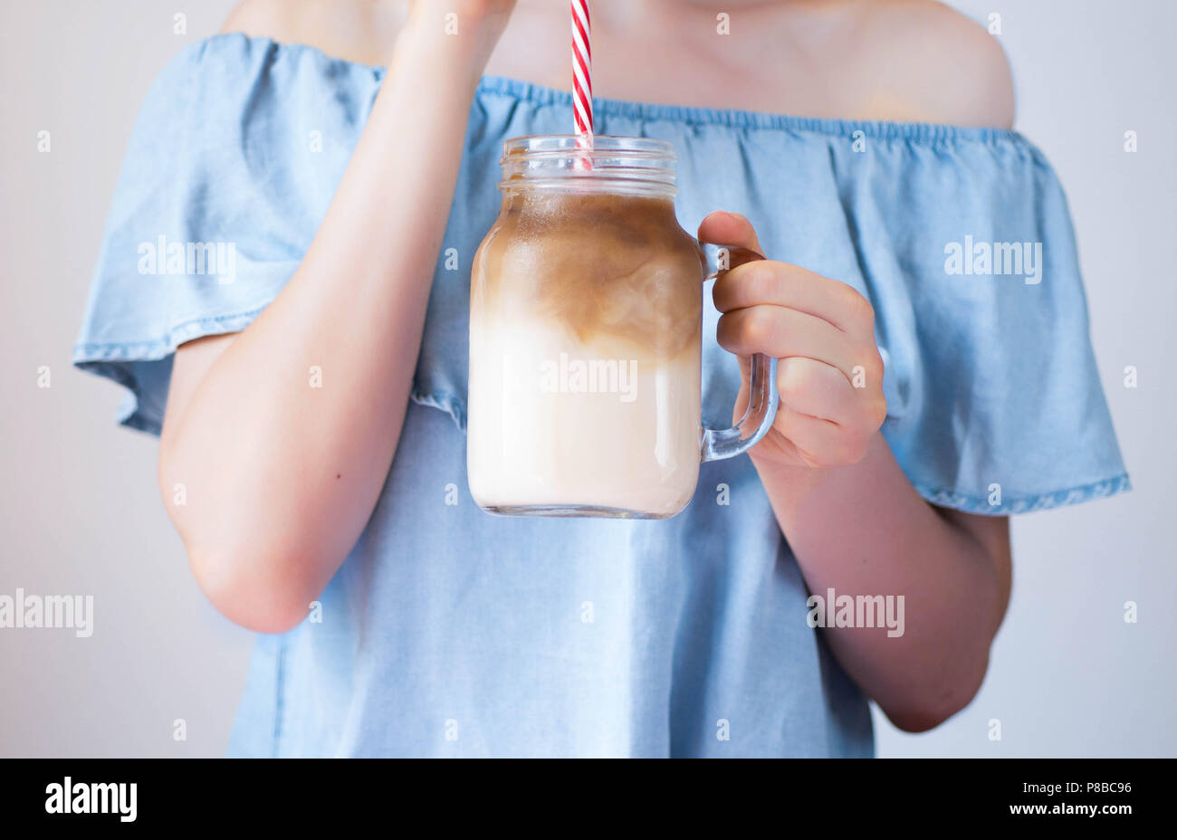 Attraente giovane donna caucasica bere caffè ghiacciato da un muratore jar tazza con una cannuccia, estate concetto di ristoro Foto Stock