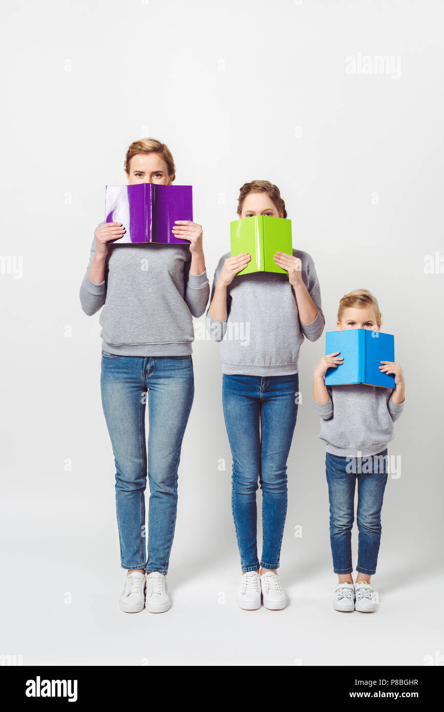 Vista offuscata della madre e le sue figlie in simili indumenti che ricoprono le facce con libri isolato su grigio Foto Stock