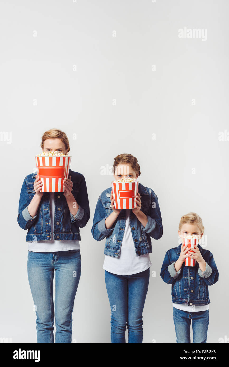 Vista offuscata della famiglia in simili abbigliamento denim facce di copertura con popcorn isolato su grigio Foto Stock