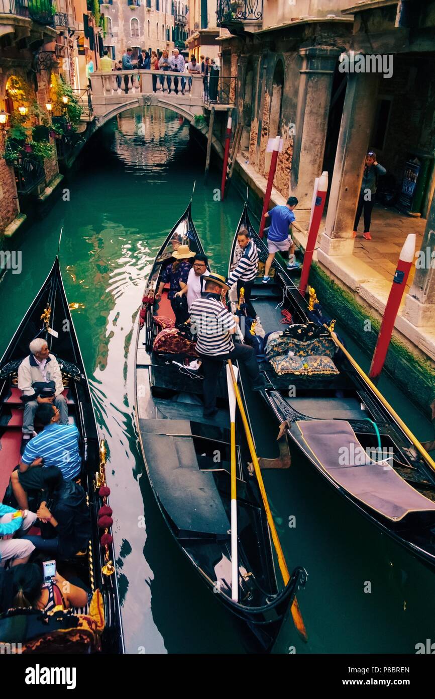 Assemblea serale delle gondole con i turisti in uno stretto canale nel cuore antico di Venezia con lanterne splendente e acqua verde smeraldo sopra visualizza Foto Stock