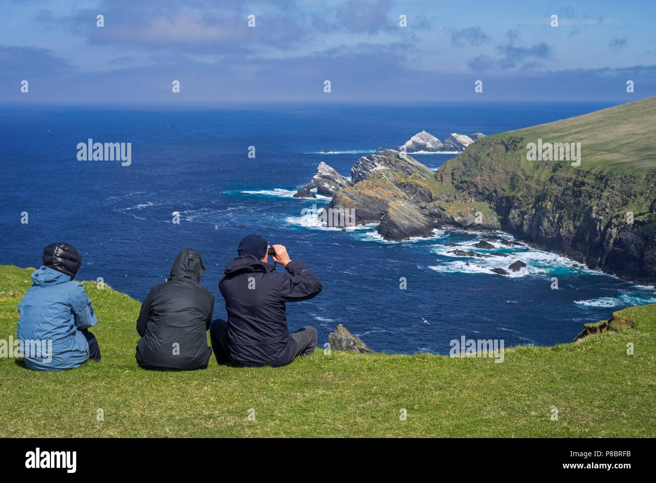 Gli amanti del birdwatching guardando la linea costiera con scogliere sul mare e pile, home all allevamento di uccelli di mare a Hermaness, Unst, isole Shetland, Scotland, Regno Unito Foto Stock