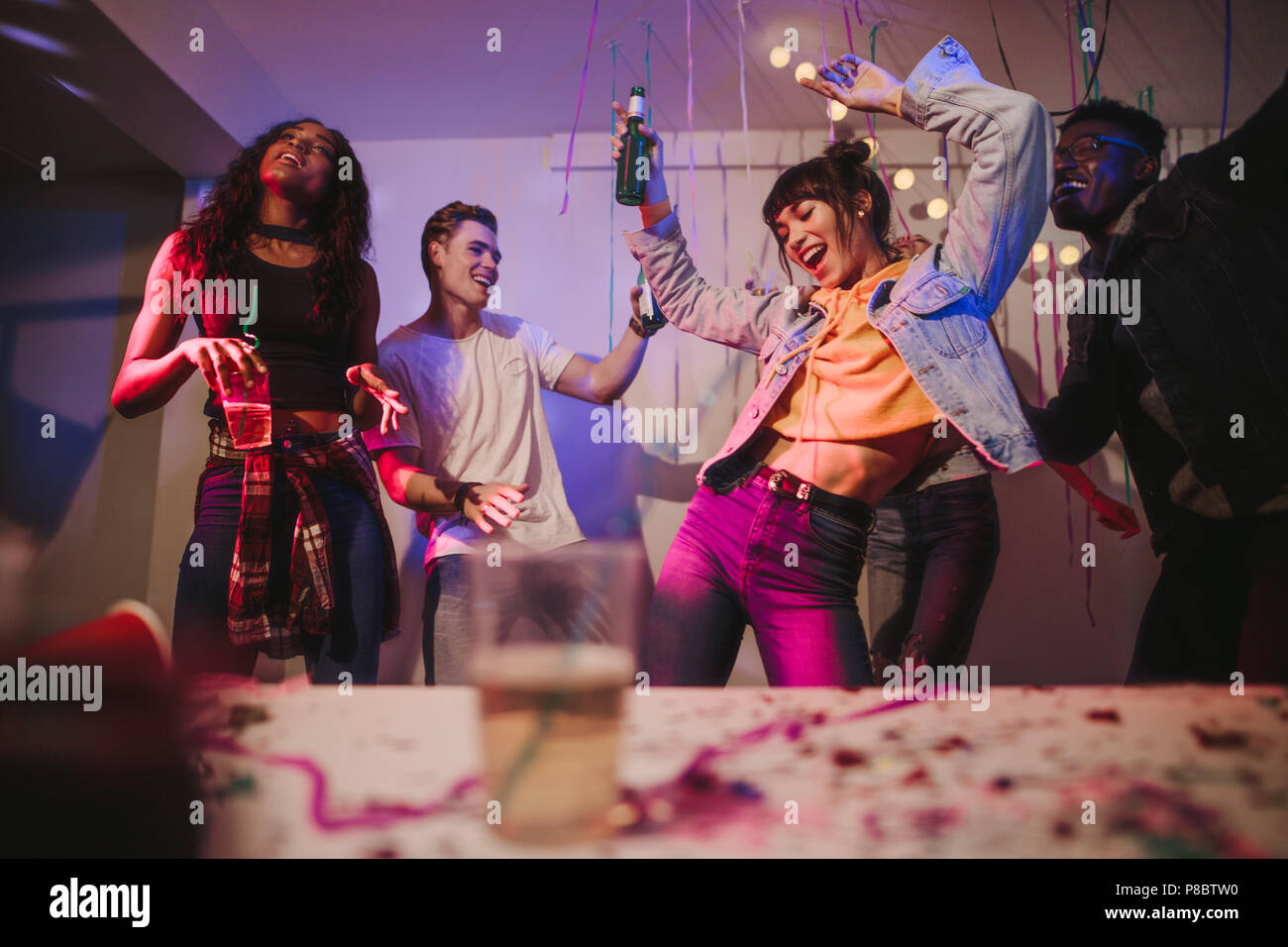 Giovani uomini e donne aventi il divertimento a un colorato house party. Amici ballare in gioia azienda bevande a house party. Foto Stock