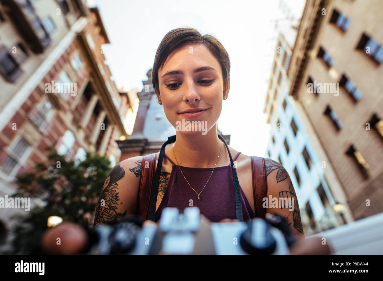 In prossimità di una donna sorridente turistica prendendo fotografia utilizzando una telecamera. Bassa angolazione di una donna prendendo foto all'aperto con edifici in background Foto Stock