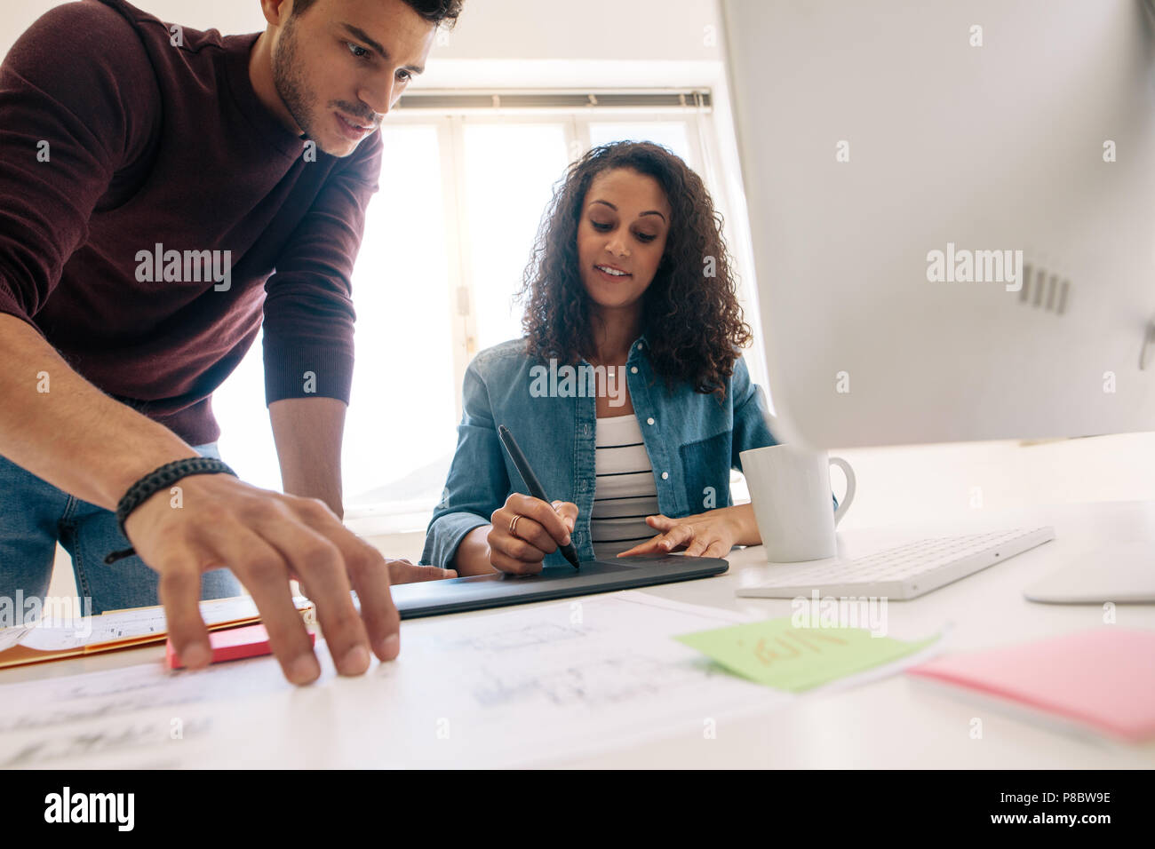 Imprenditore guardando i documenti aziendali mentre la donna è la scrittura sul blocco di scrittura digitale. Business Partner che lavorano insieme in ufficio. Foto Stock