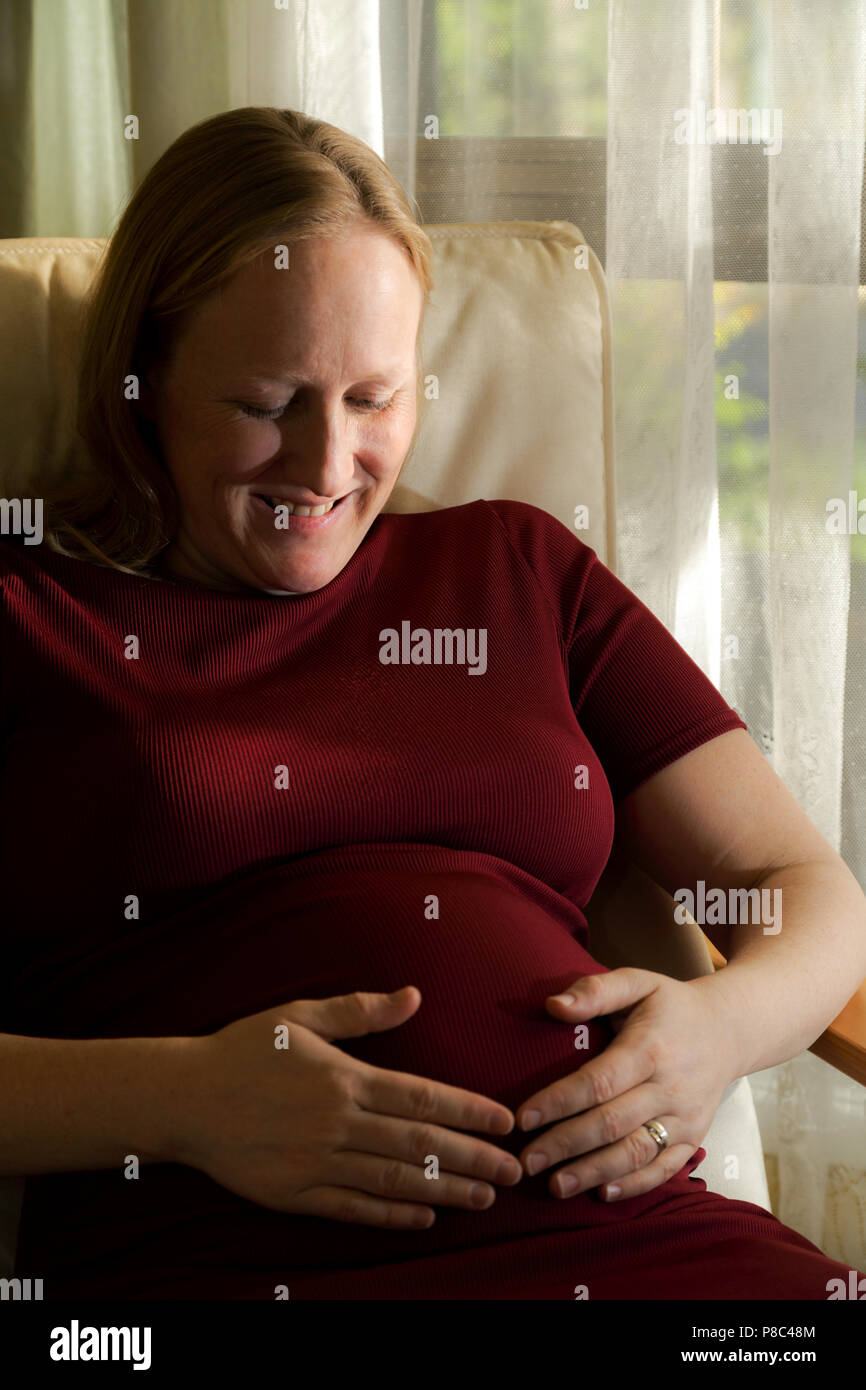 Signora bionda a metà degli anni trenta la seduta e ad accarezzarle il ventre in gravidanza. Foto Stock