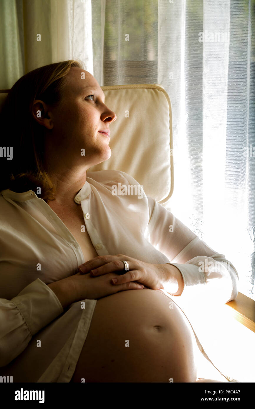 Signora bionda a metà degli anni trenta la seduta e ad accarezzarle il ventre in gravidanza. Foto Stock