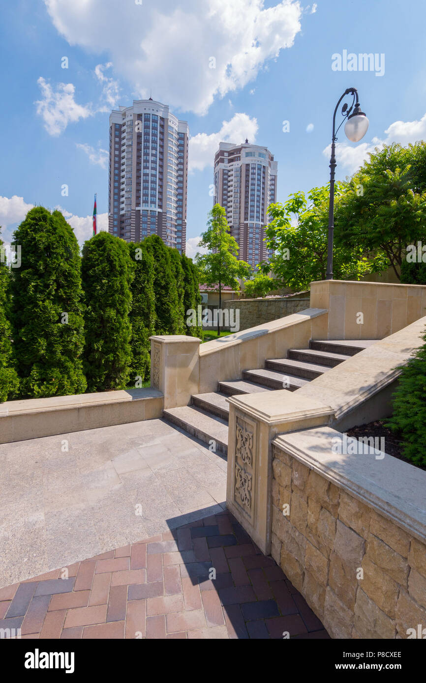 Splendida vista dalla piattaforma accanto alla scala con gradini a due edifici ad alta levatura contro uno sfondo di verdi alberi e una blu s Foto Stock