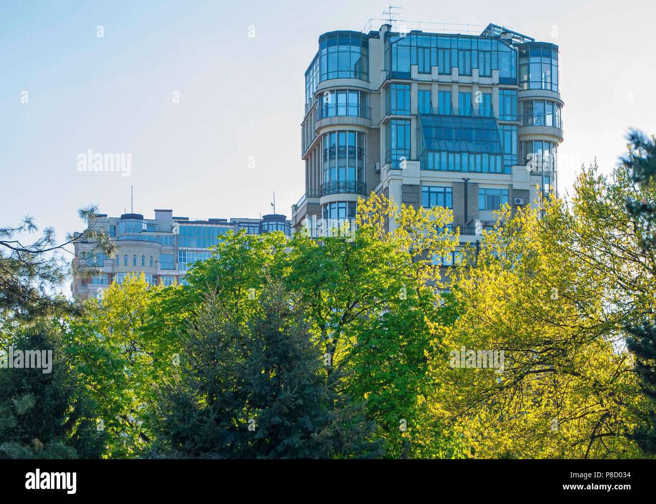 Edificio alto con molte finestre e balconi in vetro sullo sfondo delle cime di alberi con il giallo e il verde delle foglie . Per il vostro design Foto Stock