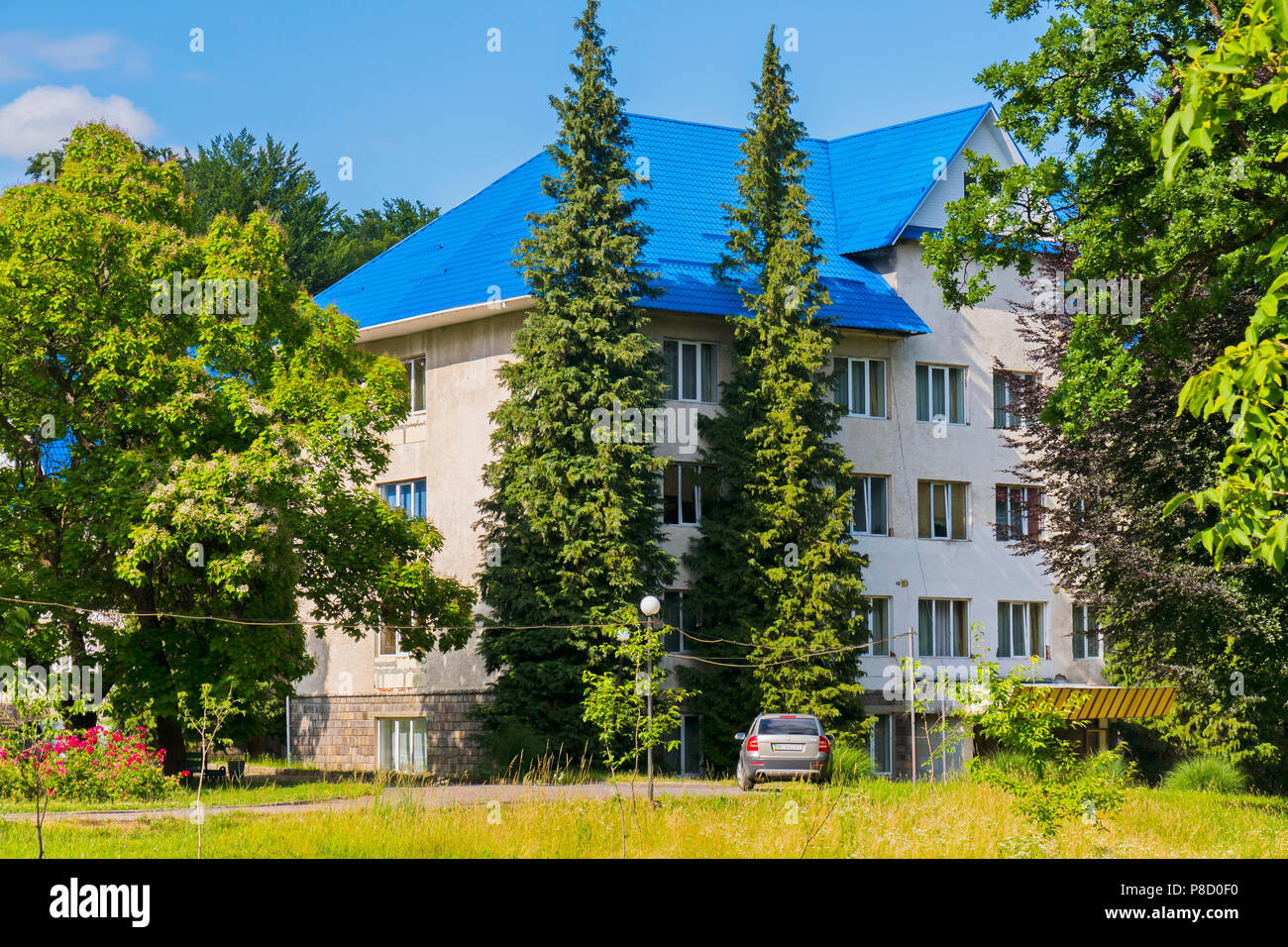 Un auto di fronte all'edificio con pareti beige e un tetto blu sullo sfondo del parco verde di zona . Per il vostro design Foto Stock