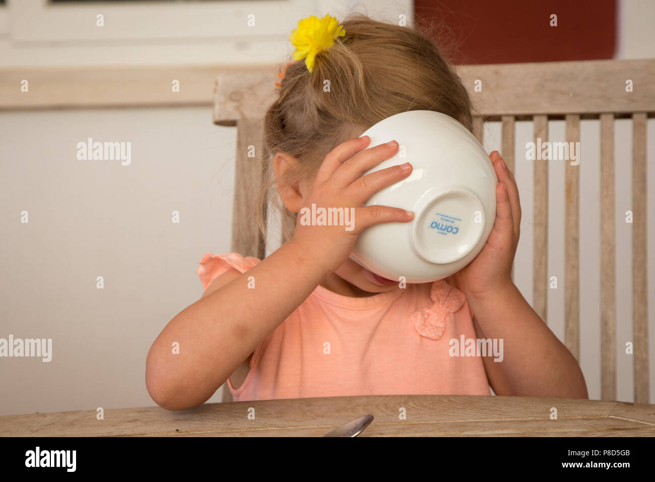 Un neonato il sollevamento di una ciotola per la sua bocca, versando gli ultimi scampoli di cereali per la sua bocca. Lei è che copre la bocca Foto Stock