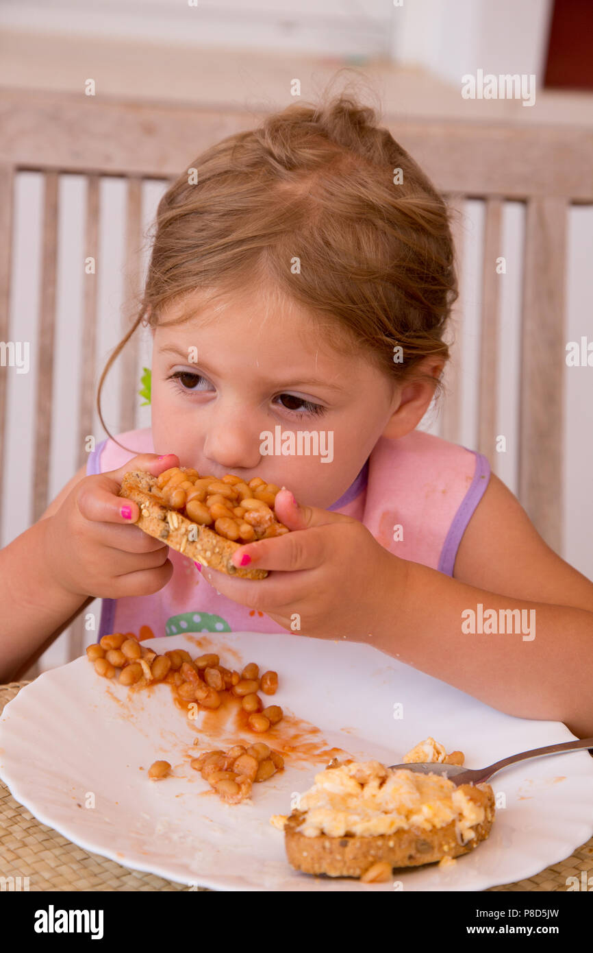 Una ragazza di due e una metà di mangiare fagioli sui toast con uova strapazzate Foto Stock