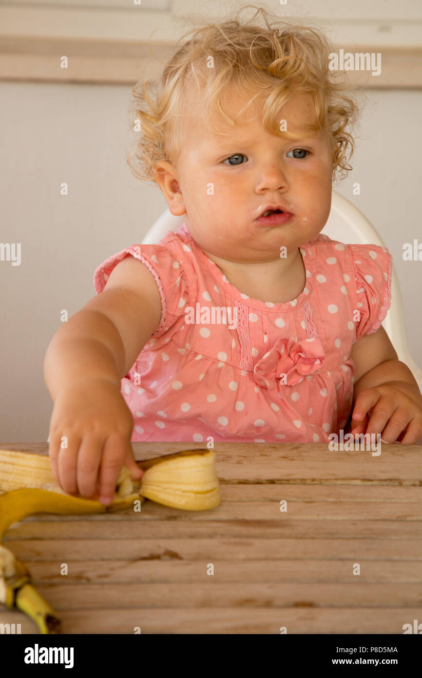 Un anno di vecchia ragazza alimentazione di se stessa una banana Foto Stock