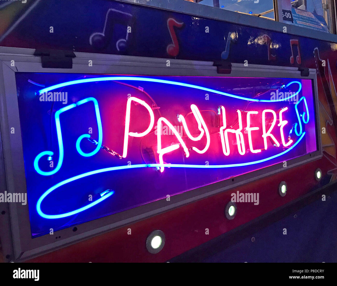 Pagare Qui insegna al neon al crepuscolo , blu, rosso, arancione neon,con nota musicale, fiera Foto Stock