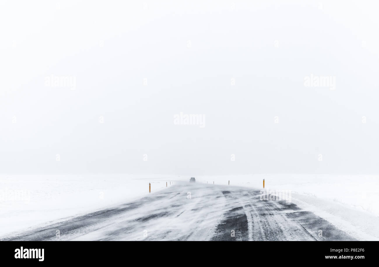 Lonely auto sulla strada gelata coperte di neve in inverno ventoso giorno, distretto di Reykjavik, Islanda Foto Stock