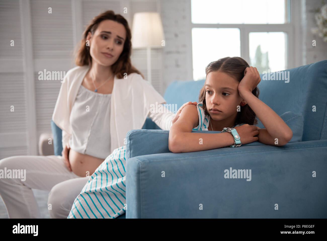 Bambina indossa orologio da polso seduto dietro la sua gravidanza madre Foto Stock