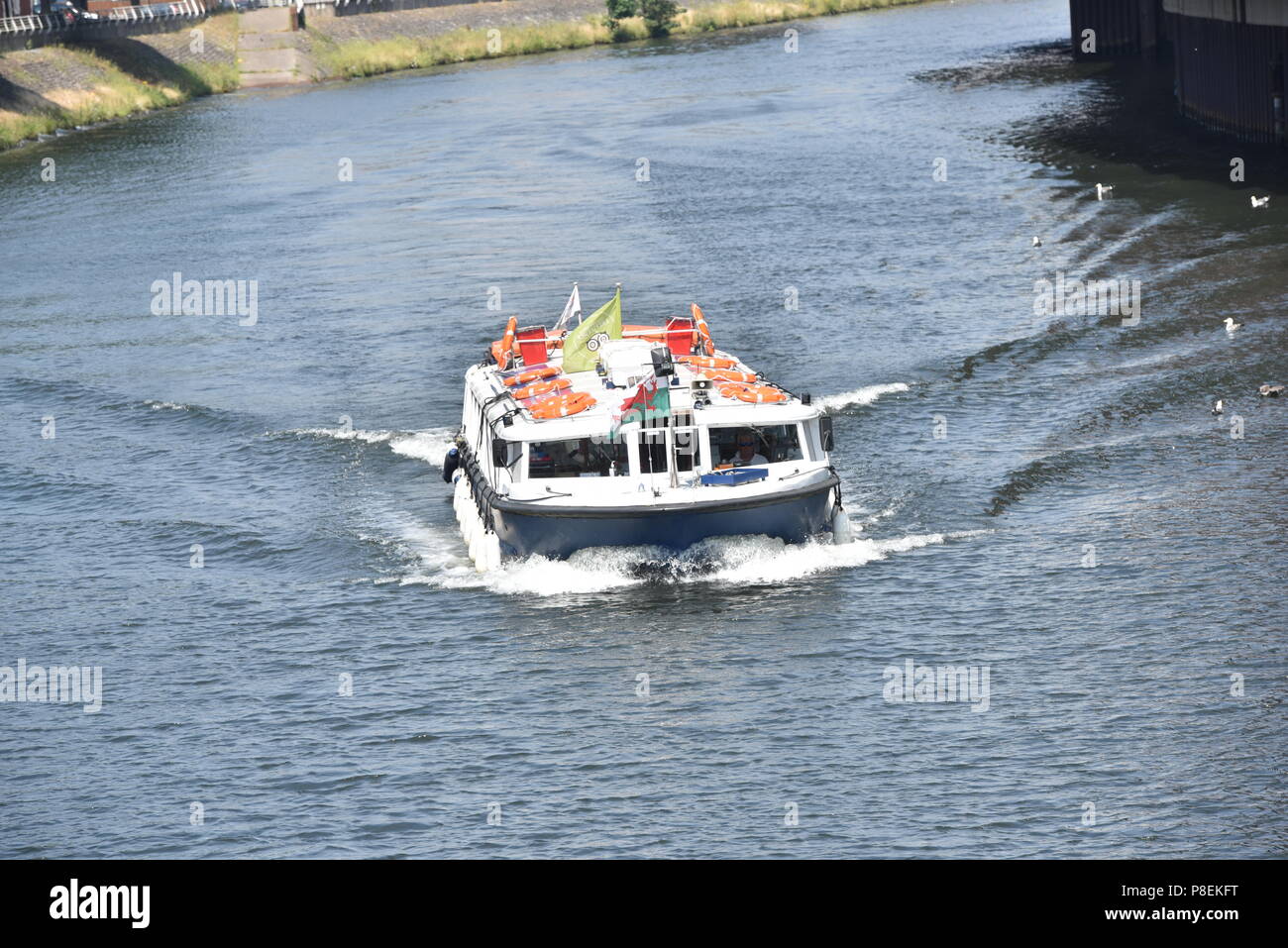 La figura mostra un autobus di acqua rendendo la sua strada giù per il fiume Taff, Cardiff, Galles del Sud, a fianco del Principato Stadium, Taffs Mead stop con Nextbike Foto Stock