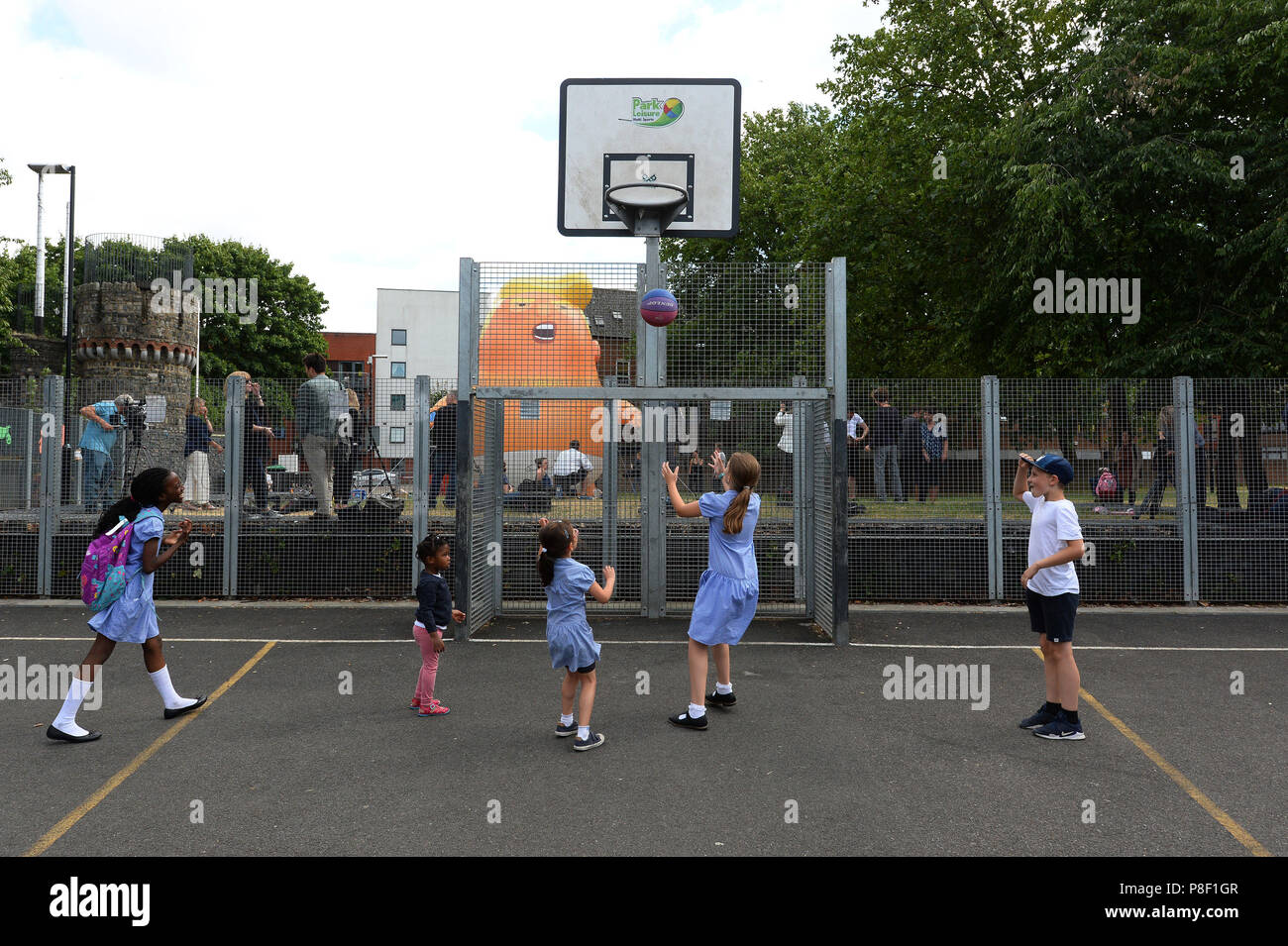 I bambini giocano a baseball di fronte al Trump Baby Blimp, mentre esso viene gonfiato durante una prova pratica, al Parco Bingfield nel nord di Londra. Foto Stock