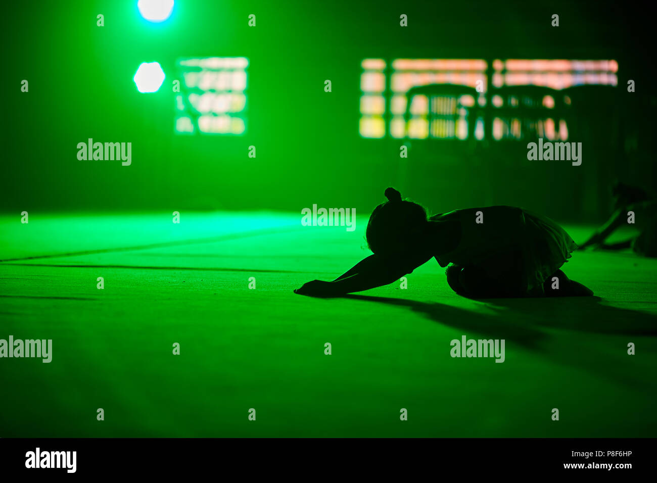 Ragazza giovane atleta ginnasta esegue elementi acrobatici in una verde luce scenica. Foto Stock