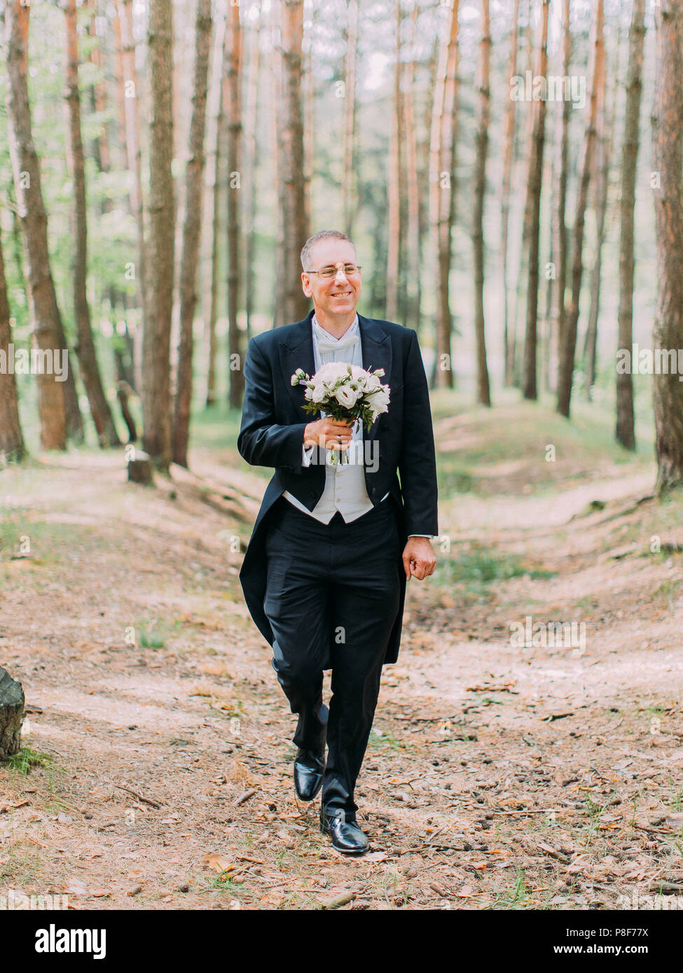 La passeggiata del bello lo sposo con il matrimonio bouquet lungo la foresta. Foto Stock