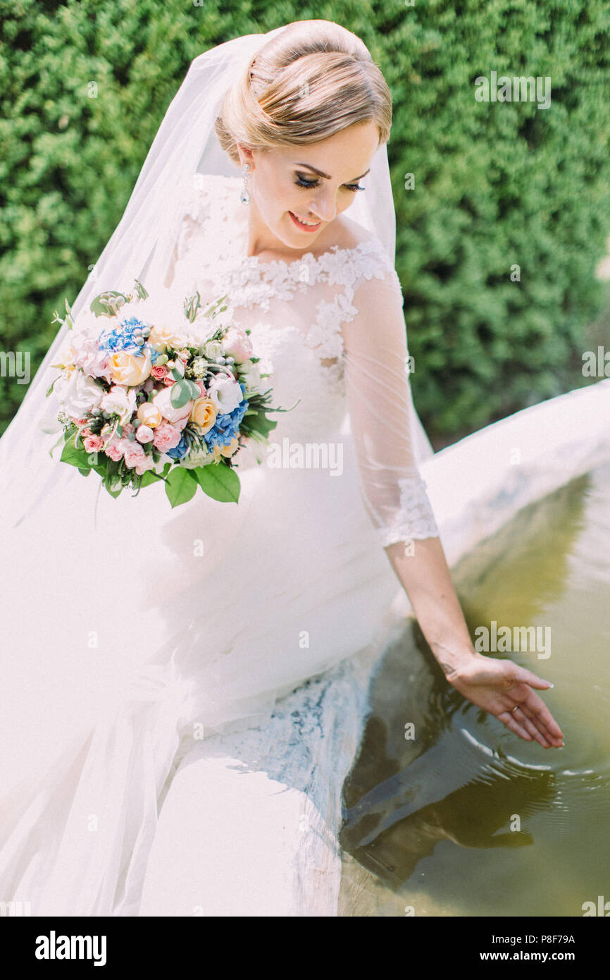 Close-up vista laterale della bella sposa giocare con l'acqua in una fontana. Foto Stock