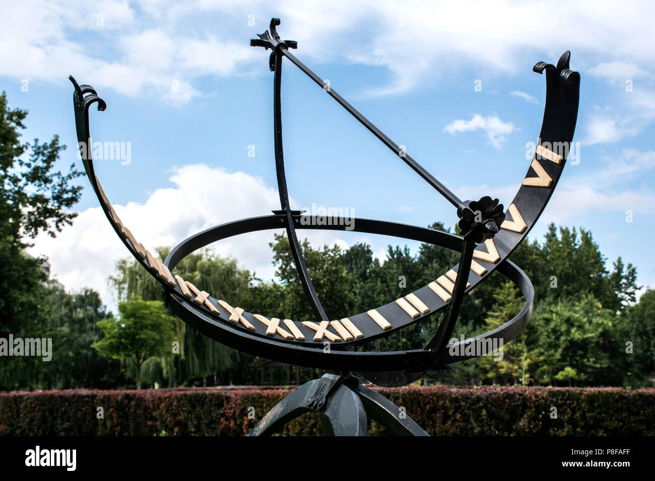 Meridiana di metallo o Orologio Solare con numeri romani in parco pubblico e cielo blu con nuvole bianche. Concetto di primavera ed estate Foto Stock