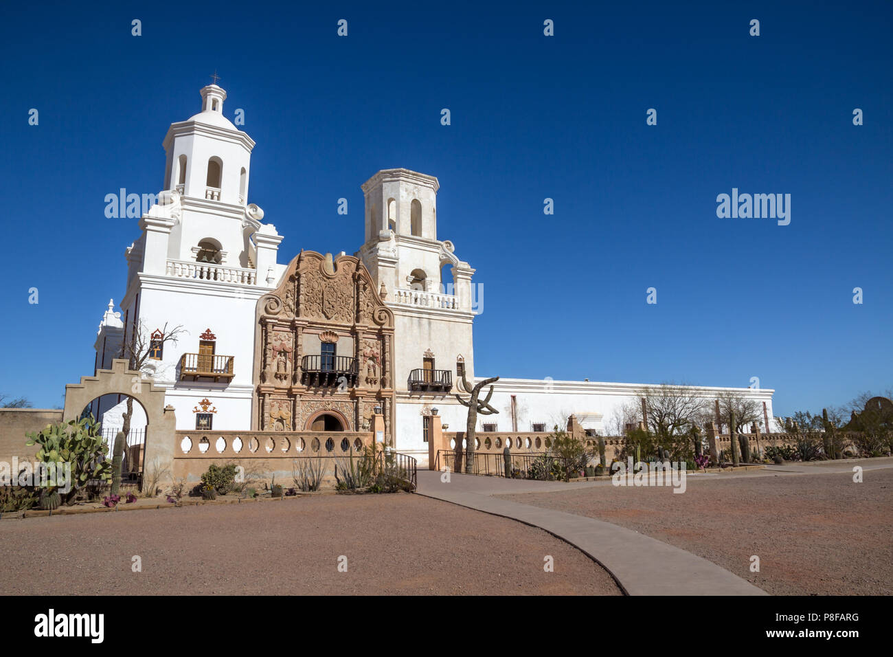 Bianca con torri e mura di San Xavier del Bac missione vicino a Tucson, Arizona, il contrasto con il profondo blu del cielo del deserto. Varie cactus crescere accanto a parete Foto Stock