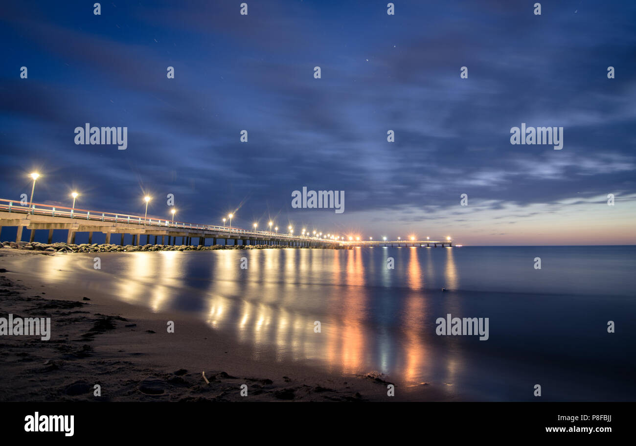 Tranquille vedute del molo del Mar Baltico durante l'alba, il tramonto e la notte con luci accese, cieli colorati e lunghi riflessi di esposizione dalla Lituania Foto Stock