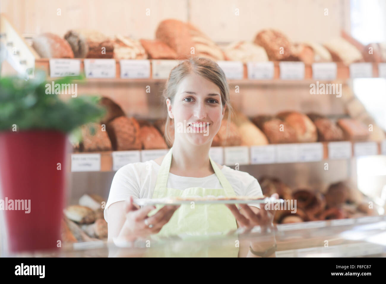 Sorridente assistente alle vendite in una panetteria tenendo un vassoio di campioni Foto Stock
