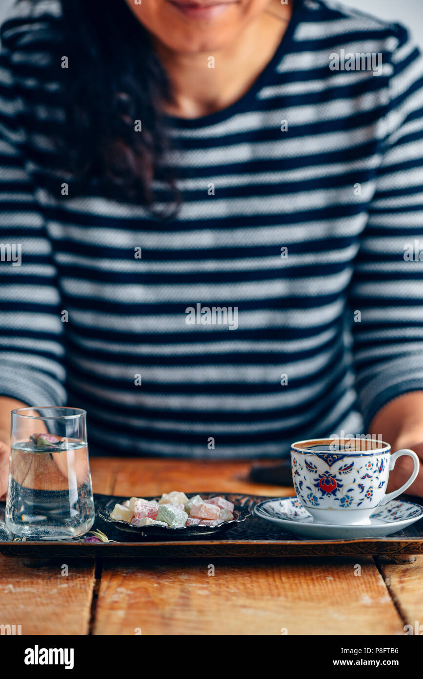 Una donna che serve il caffè turco in un tradizionale bagno turco tazza da caffè su un tradizionale in rame vassoio. Un bicchiere di acqua con un petalo di rosa all'interno e bagno turco Foto Stock