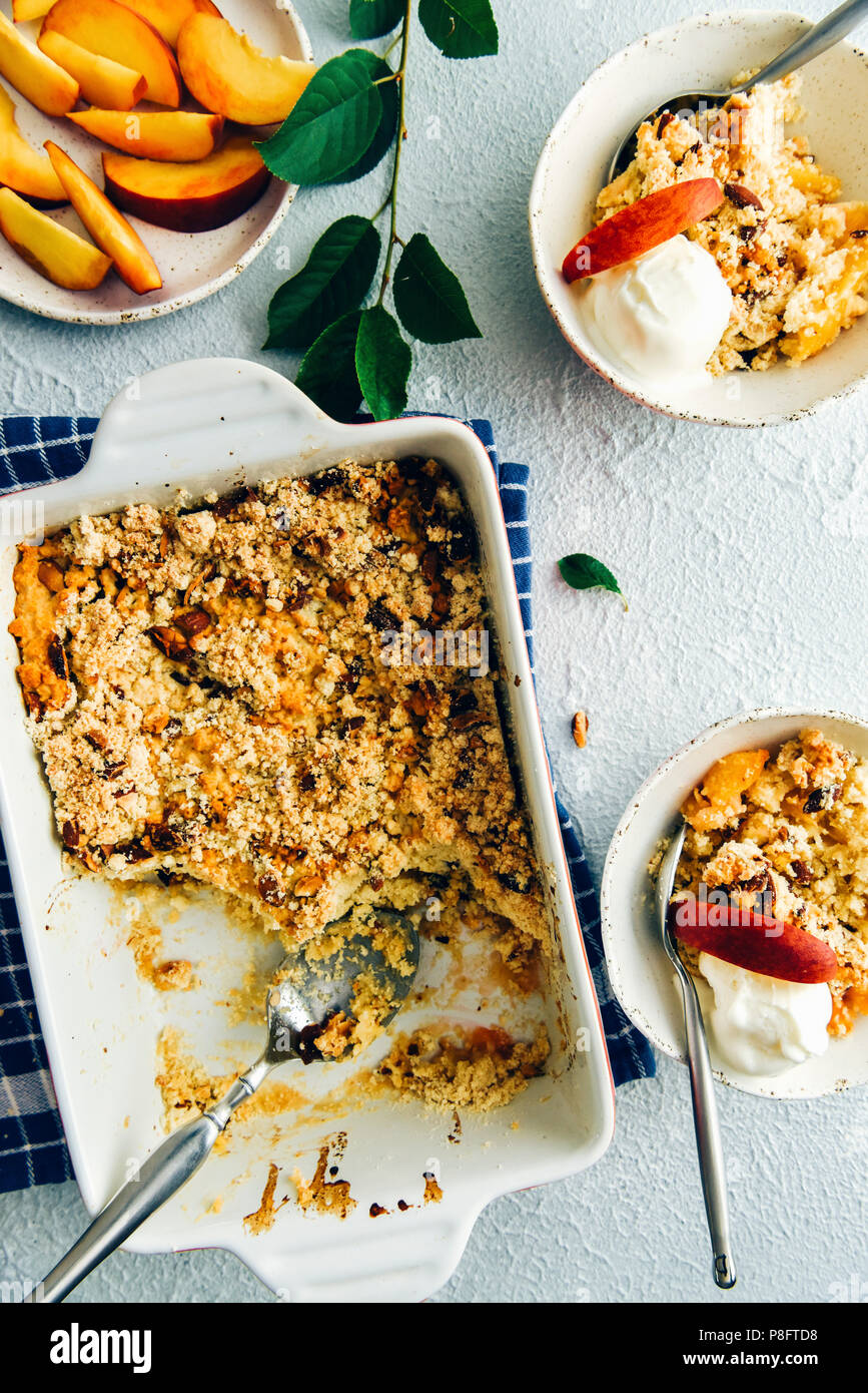 Peach cobbler in una forma rettangolare teglia da forno e in due in ceramica bianca di bocce e rabboccato con gelato alla vaniglia e fette di pesche fotografata da vista dall'alto. Pe Foto Stock