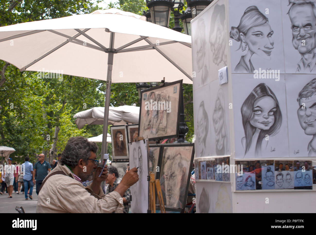 Un artista di strada seduto sotto un ombrello il disegno di una caricatura di Las Ramblas Barcellona Spagna Europa Foto Stock