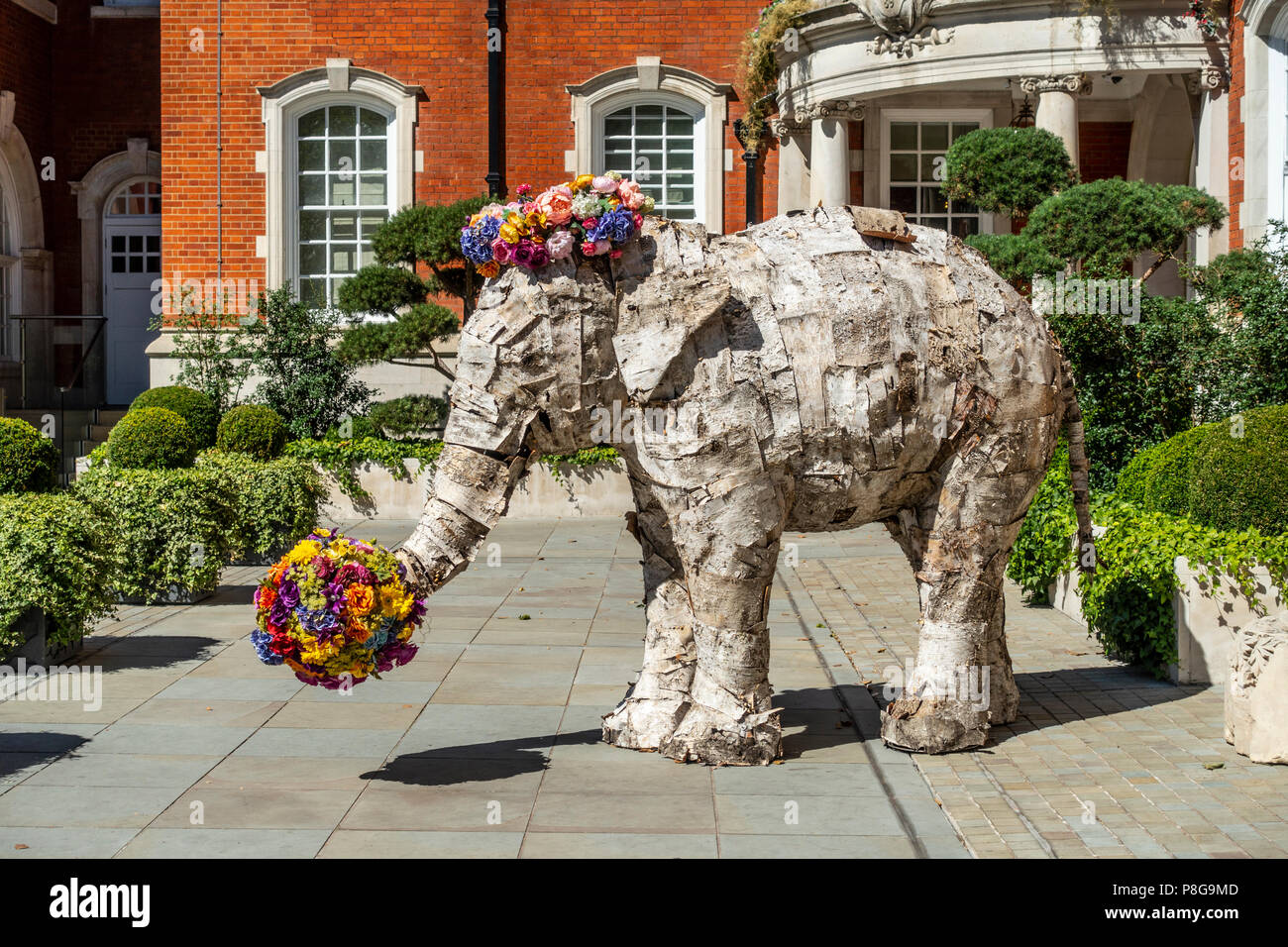 La scultura di un elefante Asiatico coperti con strisce di corteccia di albero e decorate con fiori luminosi nel giardino, vicino all'ingresso della Lalit Hotel Foto Stock